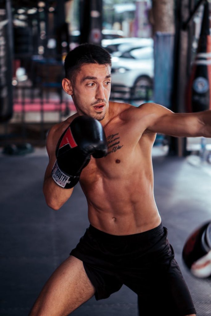 Shirtless male boxer trains intensely in a gym, showcasing strength and focus.